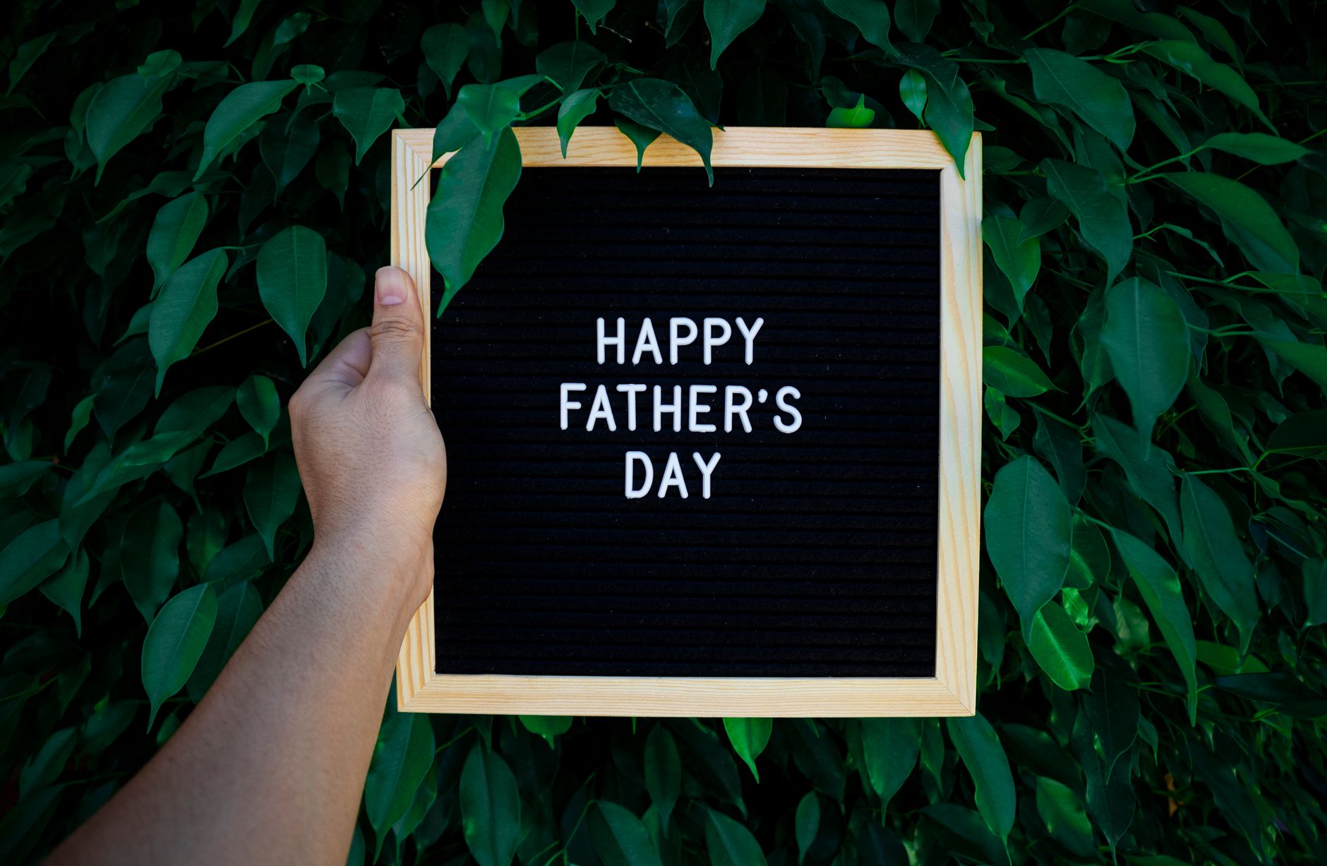 person holding a happy father s day text on wooden frame